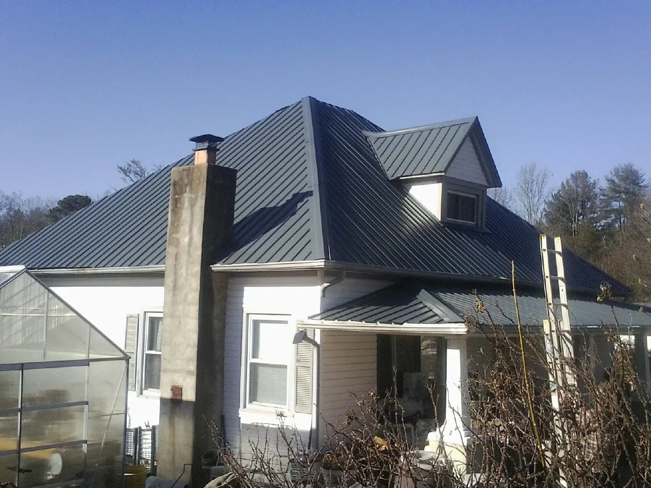 Dark blue standing seam metal roof on a white farmhouse with dormer — Slate & Tile Roof Repair by Roofing Brothers in Sugar Hill