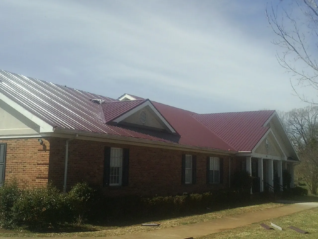 Red metal roof with gabled entries on a long brick building, from a Hail Damage Roof Repair job in Sugar Hill