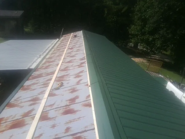 Old rusted panels beside newly installed green metal roofing — Wind Damage Roof Repair by Roofing Brothers in Sugar Hill