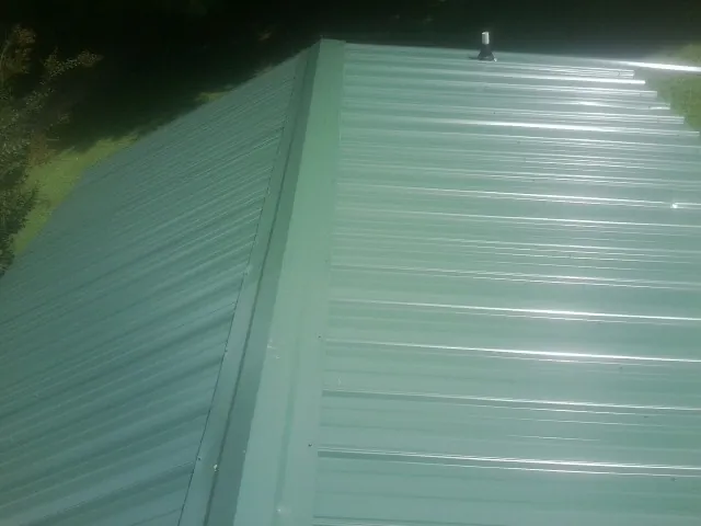 New green metal panels meeting at the ridge of a roof — Flat Roof Repair work by our crew in Sugar Hill