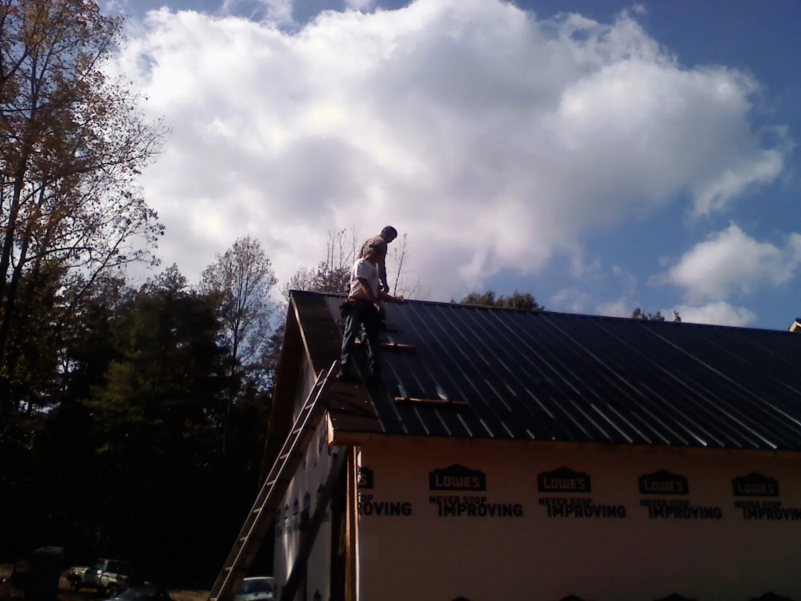 Roofer fastening dark metal panels high against a cloudy sky, from a Roof Inspection job in Sugar Hill