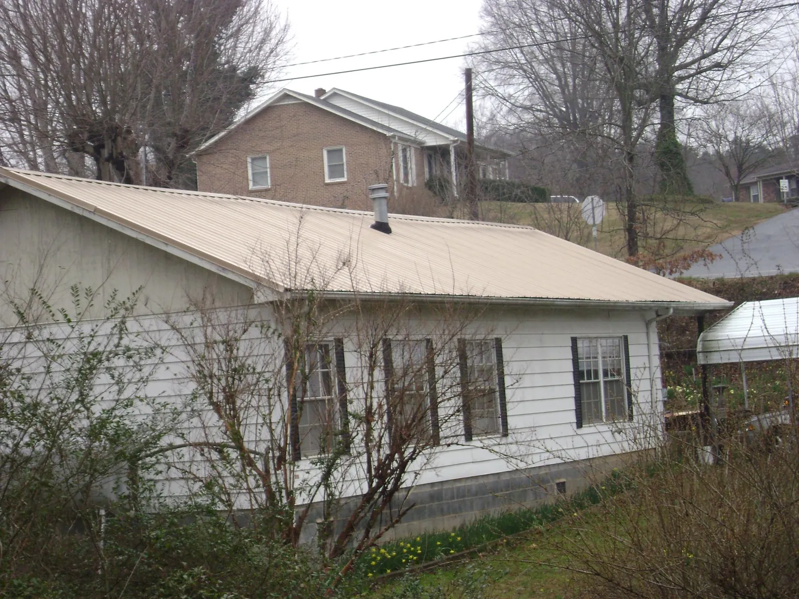Tan metal roof on a white sided house set into a hillside — Commercial Roofing by Roofing Brothers in Sugar Hill