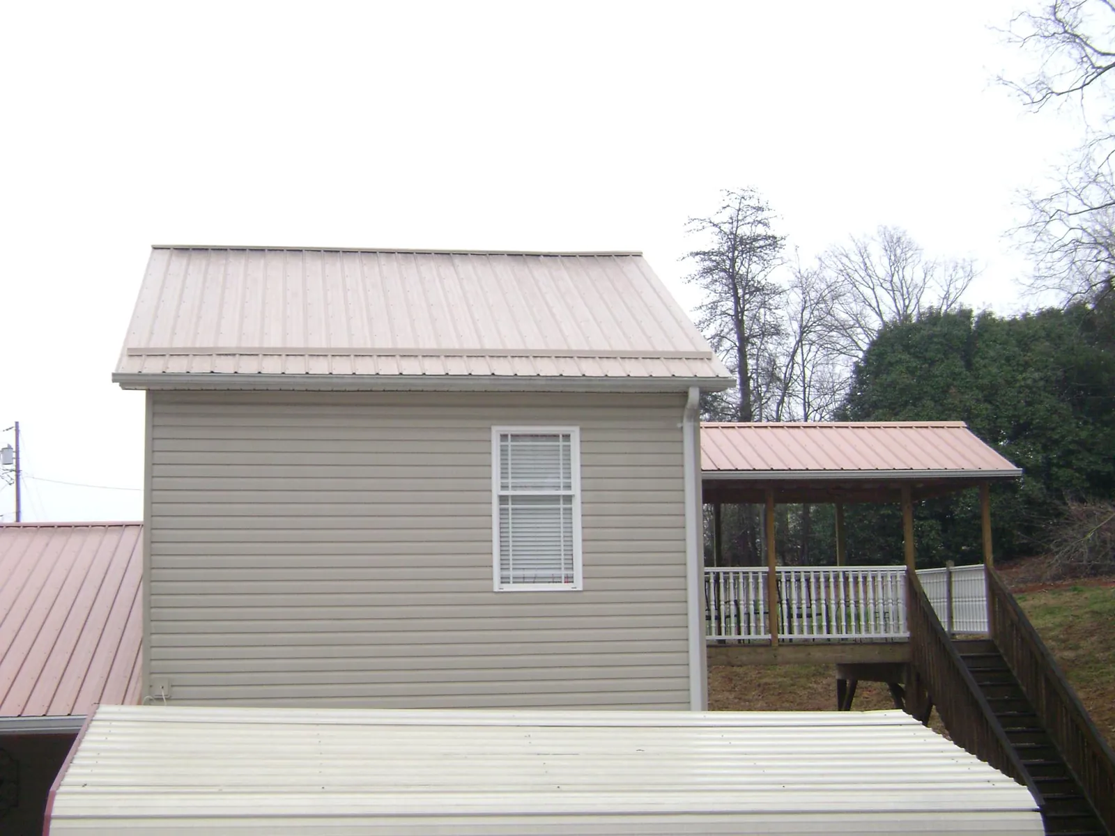 Tan metal roofs on a two story addition and attached porch, from a Roof Replacement job in Sugar Hill
